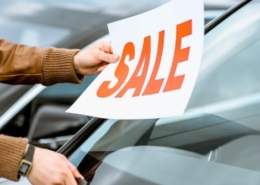 Person placing a sale sign on a used car windshield at a dealership.