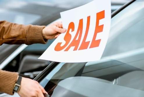 Person placing a sale sign on a used car windshield at a dealership.
