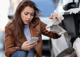 A woman checking phone after car accident damage.