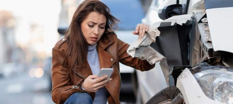 Steps to Take Immediately After a Car Accident. A woman checking phone after car accident damage.