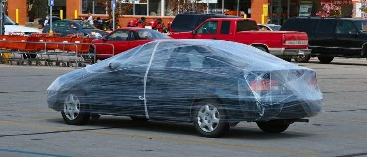A car completely wrapped in plastic wrap as part of an April Fool’s Day prank in a parking lot.