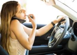 Distracted driver applying makeup while talking on the phone and steering the car.