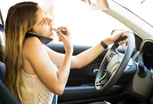 Distracted driver applying makeup while talking on the phone and steering the car.
