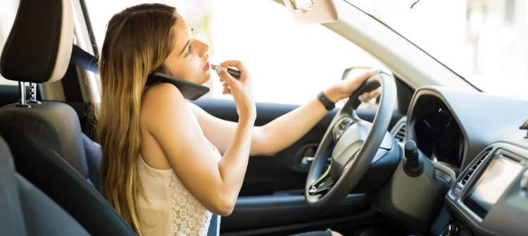 Multitasking While Driving Is a Dangerous Distraction Distracted driver applying makeup while talking on the phone and steering the car.