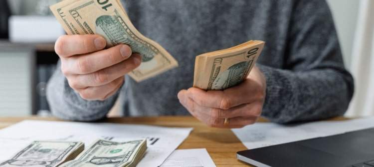 Plan Your Car Budget with Confidence – Use Our Car Affordability Calculator. A person counting money to calculate car affordability with financial charts and a calculator on the desk.