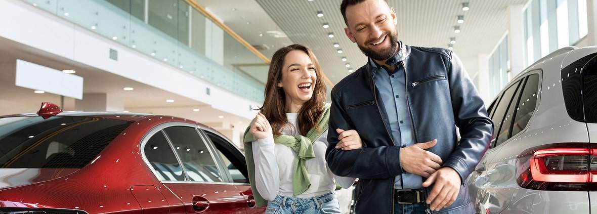 Happy couple having fun car shopping at a dealership.