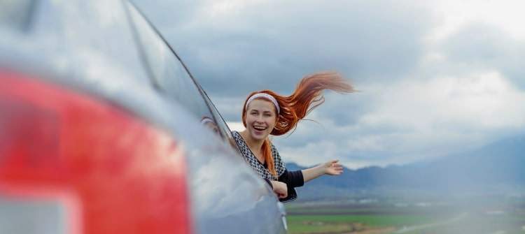 A young lady with a bubbly personality hanging out a car window.