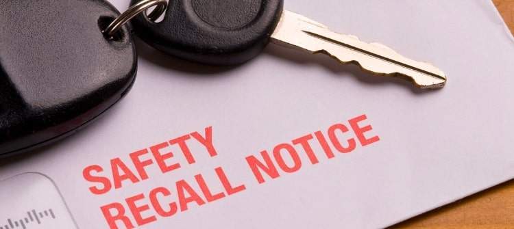 Vehicle safety recall notice in an envelope placed on a desk beside a set of car keys, symbolizing the importance of addressing automotive safety issues.