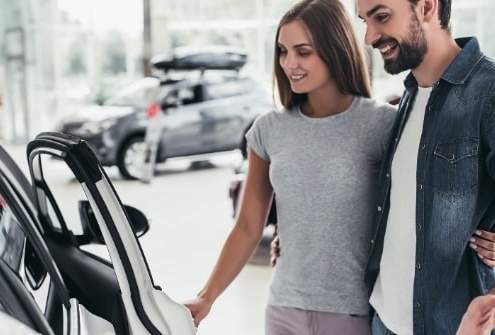 A young couple happily shopping for a new compact car in a dealership showroom.