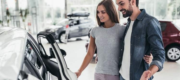 A young couple happily shopping for a new compact car in a dealership showroom.