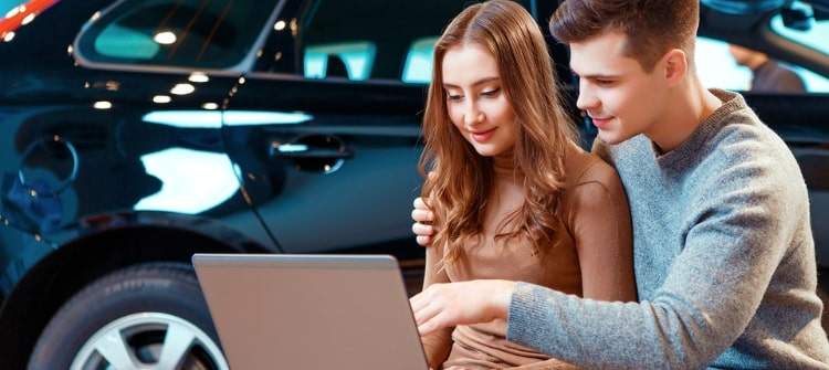Discover the Best Car-Buying Sites Online for Free New Car Quotes. A couple comparing car prices on a laptop at a dealership showroom.
