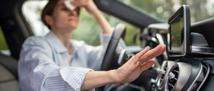 Woman sweating and struggling in a car without air conditioning on a hot summer day.