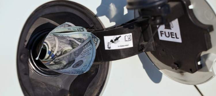 Our Gas Guzzler Calculator Will Help You Decide on a Fuel Efficient Vehicle. Cash inserted into a car's gas tank, symbolizing fuel expenses and savings.