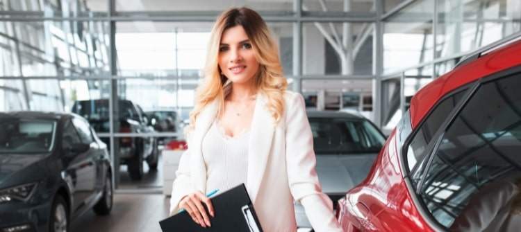 Spotting a Good Car Dealership Experience Friendly car salesperson standing next to new vehicle in dealership showroom.