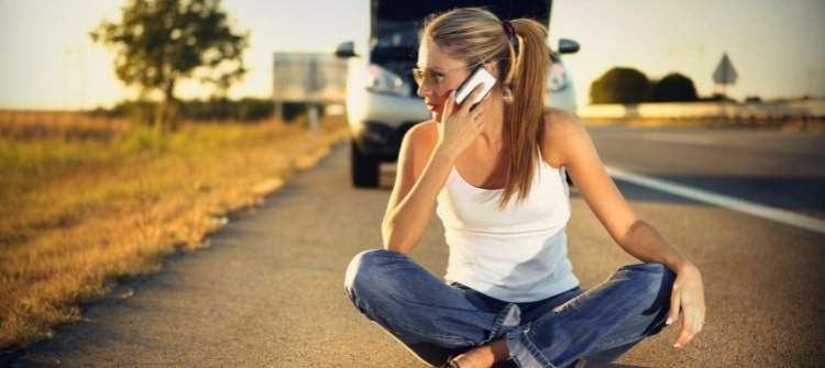 Woman stranded on highway due to car trouble. Stranded woman calling for help beside broken-down car.