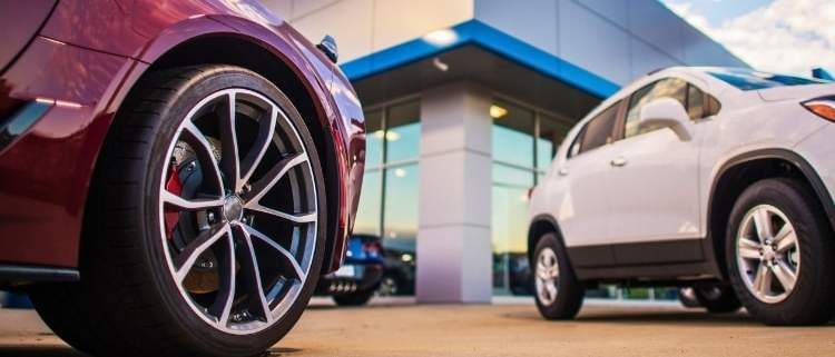 New cars parked outside a dealership, highlighting the challenges of buying a new vehicle.